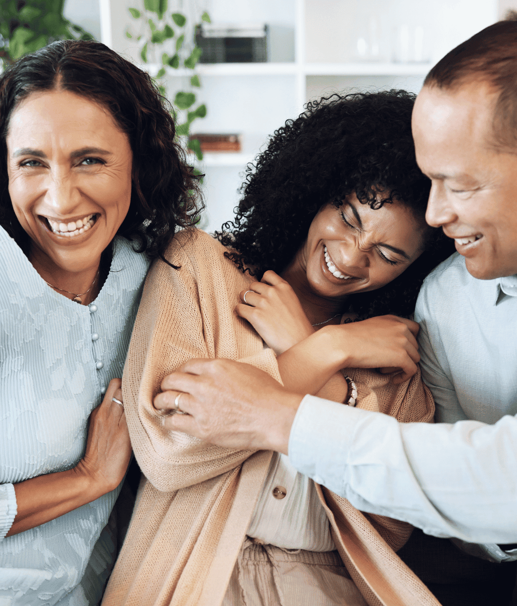 Three people laughing together while hugging tightly